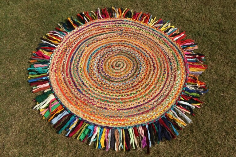 A round braided rag rug made of rainbow fabric strips with a long multicoloured fringe, laid flat on grass