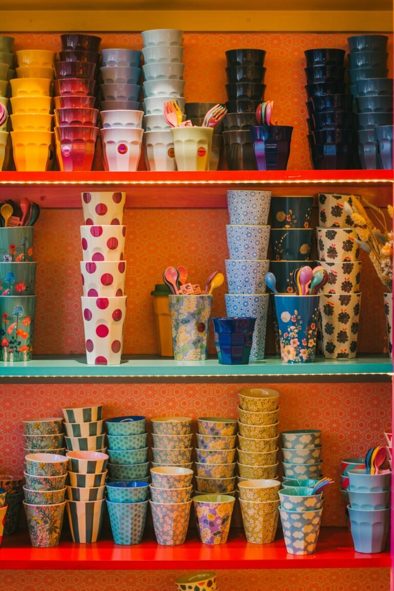 Red and teal open shelves crammed with stacks of colourful tumblers in polka dots, florals and stripes, against coral patterned wallpaper